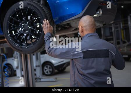 Rückansicht eines männlichen Mechanikers, der in der Garage arbeitet und das Fahrzeug untersucht Stockfoto