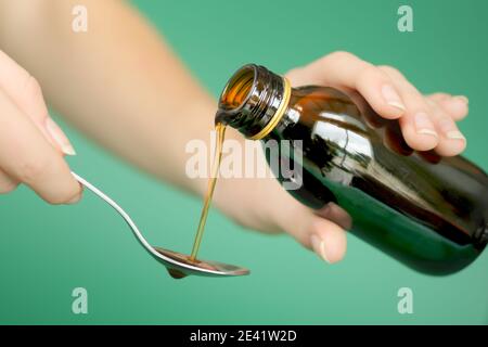 Nahaufnahme einer Hand, die Sirup aus einer Flasche Husten, Infektionen und Halsschmerzen in einen Löffel gießt. Gesundheitskonzept und Médication Stockfoto