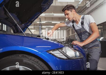 Junger männlicher Autodienstler, der Motor eines Automobils in der Garage repariert, Platz kopiert. Autotechniker, der unter der Motorhaube eines Autos arbeitet Stockfoto