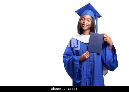 Afroamerikanische schöne Frau in einem blauen Gewand und Hut, auf einem weißen isolierten Hintergrund lächelt und zeigt Diplom Stockfoto