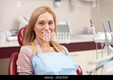 Ältere Dame, die in einem Zahnarztstuhl in der Klinik sitzt und auf einen medizinischen Termin mit ihrem Zahnarzt wartet. Fröhliche Frau mittleren Alters lächelt zur Kamera a Stockfoto