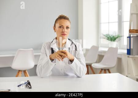 Seriöse Arzt am Schreibtisch sitzen und Blick auf die Kamera als Wenn sie ihrer Patientin zuhört Stockfoto