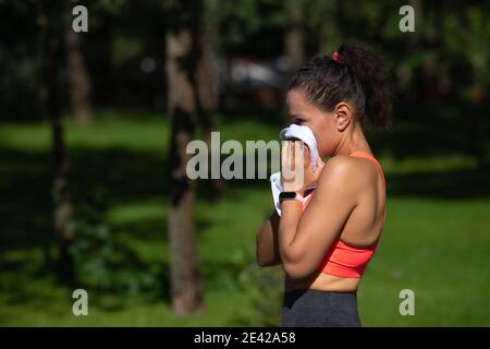 Seitenportrait einer müden jungen Frau, die nach dem Training in einem Stadtpark ihren Schweiß abwischt. Konzept des Cardio-Training im Freien Stockfoto