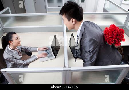 Geschäftsmann und Geschäftsfrau im Büro, Mann hält Rosen hinter dem Rücken hoch Hochwertige Fotos Stockfoto