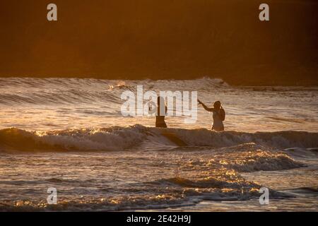 Swansea, Großbritannien. Januar 2021. Ein Paar Schwimmer trotzen dem kalten Meer, als die Sonne an Langland Bay in der Nähe von Swansea untergeht. PIC von Lisa Dawson Rees Kredit: Phil Rees/Alamy Live Nachrichten Stockfoto