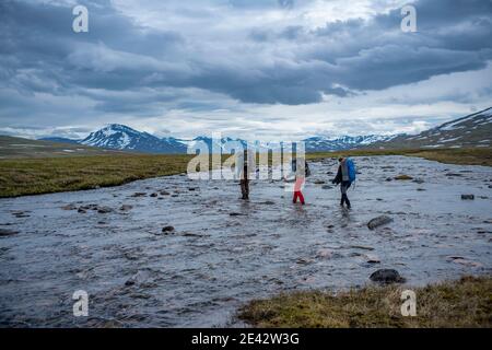 Flusslandschaft im Padjelanta Nationalpark mit Wandergruppe Freunde waten über den Fluss von Team arbeiten mit jedem Andere während der langen Wanderung in Stockfoto