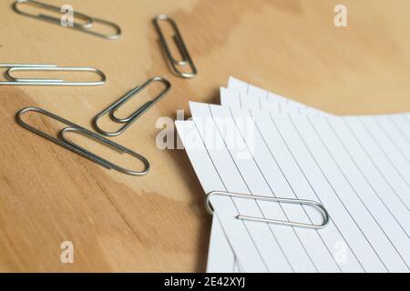 Büroklammern aus Metall und bunte Stecknadeln mit einigen Blättern Auf einem Holztisch Stockfoto