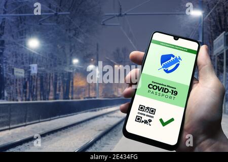 Smartphone zeigt einen gültigen digitalen Impfpass für COVID-19 in männlicher Hand, Bahnhof im Hintergrund. Impfung, Krankheit Immunität pas Stockfoto
