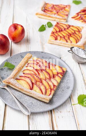 Erfrischend leckeres Dessert, saftige Nektarine Blätterteigtörtchen mit Frischkäse und bestreut mit Puderzucker auf rustikalem Holzhintergrund Stockfoto