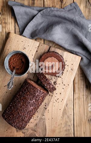 Schokoladenkuchenrolle mit Kakaofüllung, garniert mit Ganache-Glasur und bestreut auf Holzhintergrund Stockfoto