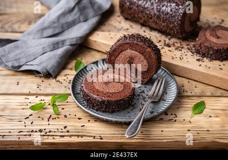 Schokoladenkuchenrolle mit Kakaofüllung, garniert mit Ganache-Glasur und bestreut auf Holzhintergrund Stockfoto