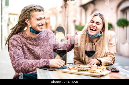 Junges Paar in der Liebe tragen offene Gesichtsmaske Spaß haben An der Weinbar draußen - Fröhliche, moderne Liebhaber, die Mittagessen Gemeinsam im Restaurant dehor Stockfoto