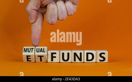 Investmentfonds vs. ETF-Symbol. Geschäftsmann dreht einen Würfel und ändert Wörter 'ETF, Exchange-Traded Fund' in 'Utual Funds. Schöner orangefarbener Hintergrund, Kopie Stockfoto