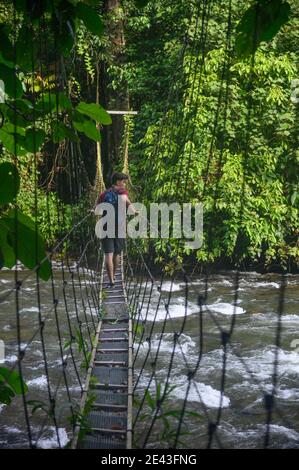 Junger Mann, der über eine Hängebrücke im Dschungel über eine Fluss Stockfoto