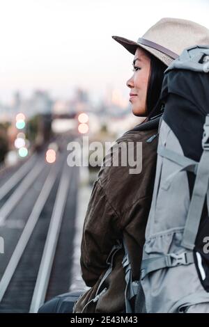 Rückansicht der erfreut asiatische weibliche Backpacker sitzt auf Hintergrund Der Eisenbahn und Blick weg über Schulter während des Abenteuers in Australien Stockfoto