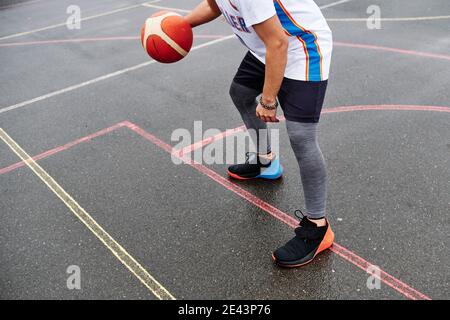 Zugeschnittenes Bild eines nicht erkennbaren Mannes, der auf dem Platz Basketball spielt. Sportkonzept. Stockfoto