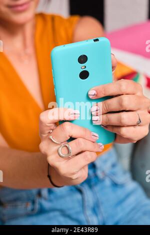 Junge Frau, die Selbstporträt auf blauem Handy, während Sitzen auf Sofa in stilvollen Raum mit gestreiften Wand und Retro-Telefonempfänger Stockfoto