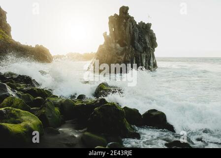 Spektakuläre Landschaft mit schäumenden Wellen, die gegen raue Felsformationen plätschern Bedeckt mit Moos bei Sonnenuntergang an der Küste Teneriffas Insel in Spanien Stockfoto