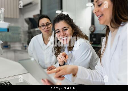 Junge weibliche Apotheker Forscher versammeln sich am Tisch mit Laptop mit Diagramme und Diskussion der Ergebnisse der Forschung während der Zusammenarbeit in Wissenschaftlich Stockfoto