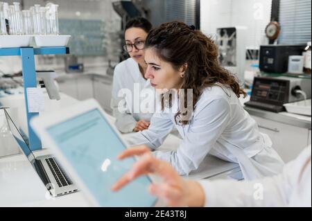Junge weibliche Apotheker Forscher versammeln sich am Tisch mit Laptop mit Diagramme und Diskussion der Ergebnisse der Forschung während der Zusammenarbeit in Wissenschaftlich Stockfoto