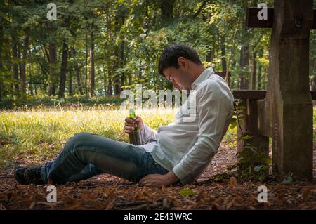 Deprimierter betrunkener Mann liegt auf dem Boden in der Nähe der Parkbank Mit einer Bierflasche Stockfoto