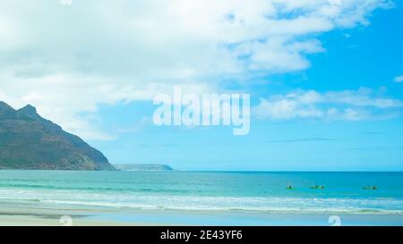 Hout Bay- Kapstadt, Südafrika - 19-01-2021 Menschen Kanufahren in leuchtend grünen Kanus. Wolkiger Himmel im Hintergrund. Stockfoto