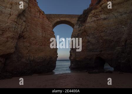 Massive Felsklippen verbunden mit Bogen auf Praia de Estudantes Sandstrand des Ozeans gegen wolkenlosen Abendhimmel in Algarve Stockfoto