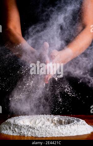 Gesichtslose weibliche Bäckerin klatscht Hände in Mehl, während sie Brot macht Teig mit Weizenmehl und Eiern am Tisch Stockfoto
