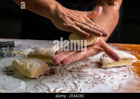 Hoher Winkel der gesichtslosen Bäcker Kneten und Formen von Bällen Teig, der Brot am Holztisch in Mehl macht Stockfoto