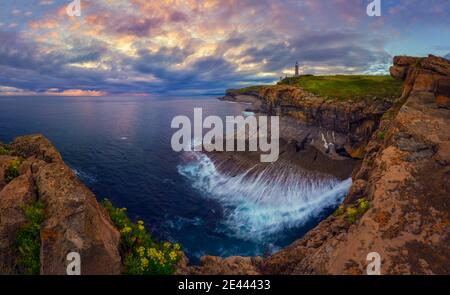 Landschaftlich schöne Aussicht auf kleine Insel mit Leuchtturm genannt Faro de Cabo Mayor mit Küste durch Brücke unter dramatischen bewölkt verbunden Himmel bei Sonnenuntergang in S Stockfoto