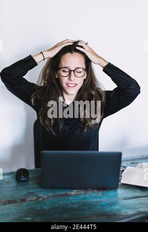 Frustriert junge weibliche Remote-Mitarbeiter in Brille berühren Kopf und Blick auf Laptop-Bildschirm, während immer Problem während der Telearbeit aus Heimbüro Stockfoto
