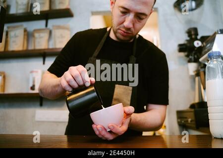 Nahaufnahme eines Kellners, der Milch zu einer Tasse serviert Kaffee Stockfoto