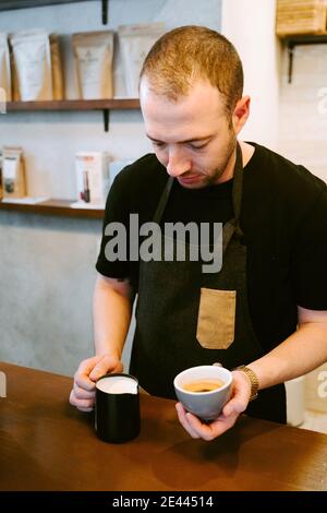 Nahaufnahme eines Kellners, der Milch zu einer Tasse serviert Kaffee Stockfoto