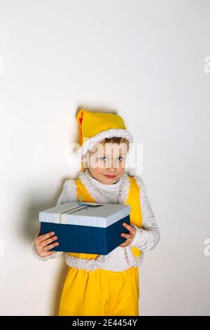 Portrait von niedlichen Baby junge in gelb gnome elf Outfit Mit lustigen Hut und Weste mit großen blauen Geschenk Feld Stockfoto