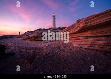 Herrliche Aussicht auf den Leuchtturm auf einem Hügel in der Nähe des Meeres gegenüber Farbenprächtiger Sonnenuntergang in Cadiz Stockfoto