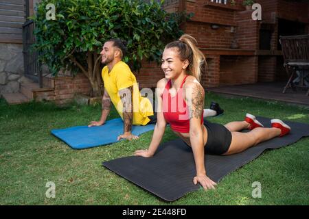 Begeistert fit Sportlerin und Sportler üben Yoga in Bhujangasana und Stretching Körper auf Matten im Hinterhof Stockfoto