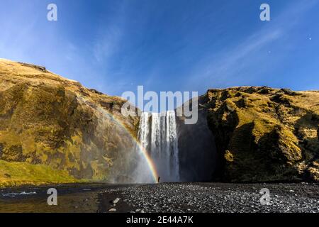 Unerkennbarer Reisender, der in der Nähe von erstaunlichen Wasserfällen und Regenbogen in den Bergen steht Während des Urlaubs in Island Stockfoto