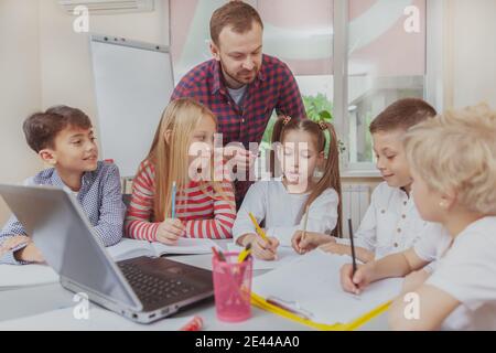 Grundschullehrer genießen die Arbeit mit fröhlichen kleinen Kindern. Gruppe von Vorschulkindern, die während des Kunstunterrichts sprechen Stockfoto