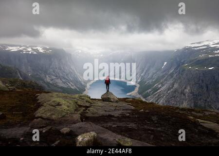 Abstand Rückansicht des Explorers stehend am Rand von Trolltunga Felsformation an einem bewölkten Tag während des Urlaubs in Norwegen Stockfoto