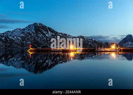 Malerische Aussicht auf hölzerne Piers im Hafen mit beleuchteten Lampen Das Hotel liegt in der Nähe von Meer in bergigen Gelände am Abend in Norwegen Stockfoto