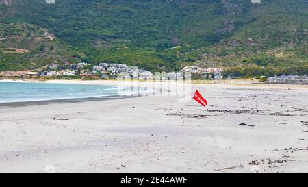 Hout Bay- Kapstadt, Südafrika - 19-01-2021 leuchtend rote 'No Swimming' Flagge weht im Wind am Hout Bay Strand. Stockfoto