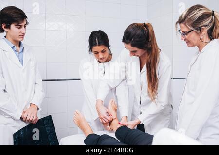 Zwei Ärzte untersuchen das Bein eines Patienten Liegt auf einer Bahre auf einem Krankenhauszimmer während Ein anderer hält eine Röntgenaufnahme Stockfoto