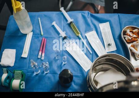 Operationstisch mit blauer Tischdecke mit gefüllten Nadeln, gebrauchter Jodgaze, Anästhesie und einem Metalltopf unter anderem Stockfoto