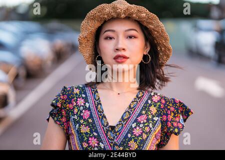 Asiatische Frau in Strohhut und mit Weidenhandtasche stehend Auf dem Parkplatz und Blick auf die Kamera Stockfoto