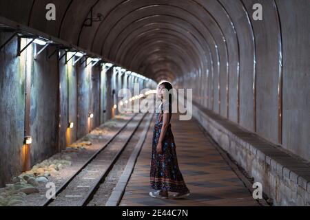 Seitenansicht der asiatischen Frau im Maxi-Kleid im Stehen Alter Baiji Tunnel in Taiwan und Blick auf die Kamera Stockfoto