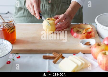 Unkenntliche Person schneidet geschälten Apfel auf Schneidebrett in der Nähe von Honig Mit Mehl und Butter mit Zimt während der Zubereitung Stockfoto