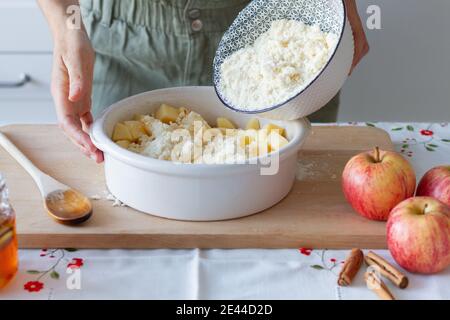 Unkenntliche Person, die Krümel hinzugibt, um Äpfel in der Backform zu schneiden In der Nähe von Honig und Zimt beim Kochen bröckeln zu Hause Stockfoto