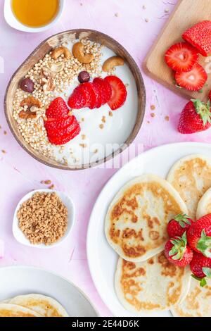 Draufsicht auf den Tisch mit Schale Müsli und Joghurt Und hausgemachte Pfannkuchen mit Erdbeeren serviert zum leckeren Frühstück in Morgen Stockfoto