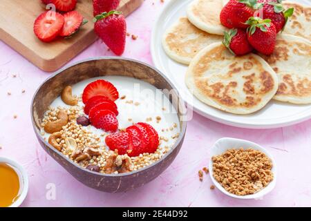 Draufsicht auf den Tisch mit Schale Müsli und Joghurt Und hausgemachte Pfannkuchen mit Erdbeeren serviert zum leckeren Frühstück in Morgen Stockfoto