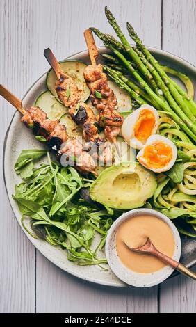 Blick von oben auf leckeres Hühnerfleisch auf Holzspieße geschnürt Auf Teller mit Sauce und verschiedenen Zutaten Stockfoto